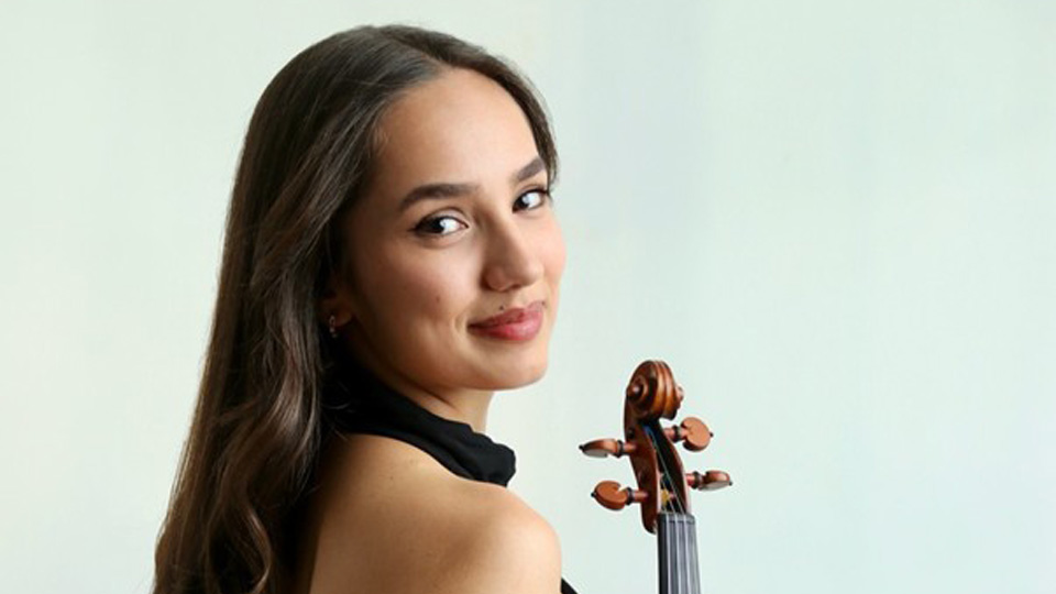 A women with dark brown hair, with a black dress, holding a violin.